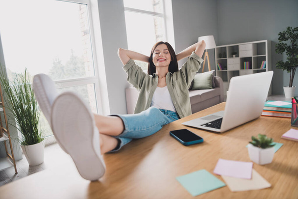 Full length photo of delighted positive lady sit chair put legs table hands behind head closed eyes accomplish task office indoors. - Fotoğraf, Görsel