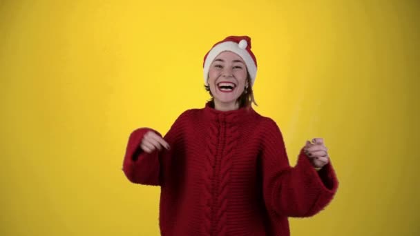 Young positive woman in christmas santa hat isolated over yellow background. Happy young woman in Santa hat is dancing. People and winter holidays concept - Footage, Video