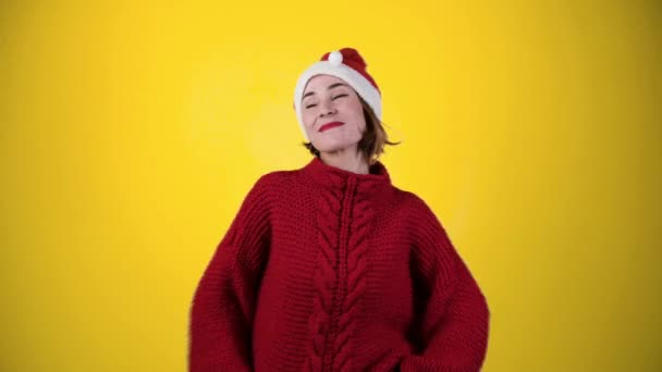 Молодая позитивная женщина в рождественской шляпе Санта изолирована на жёлтом фоне. Счастливая молодая женщина в шляпе Санты танцует. Концепция зимнего отдыха - Кадры, видео