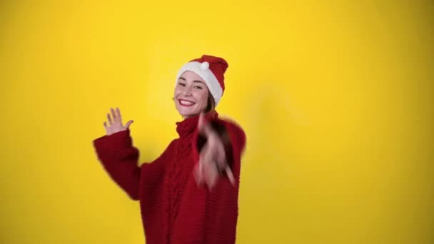 Młoda pozytywna kobieta w świątecznym kapeluszu odizolowana na żółtym tle. Szczęśliwa młoda kobieta w kapeluszu Mikołaja tańczy. Koncepcja ludzi i ferie zimowe - Materiał filmowy, wideo
