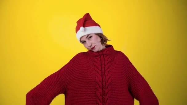 Jonge positieve vrouw in kerstmis santa hoed geïsoleerd over gele achtergrond. Gelukkige jonge vrouw met kerstmuts danst. Mensen en wintervakantie concept - Video