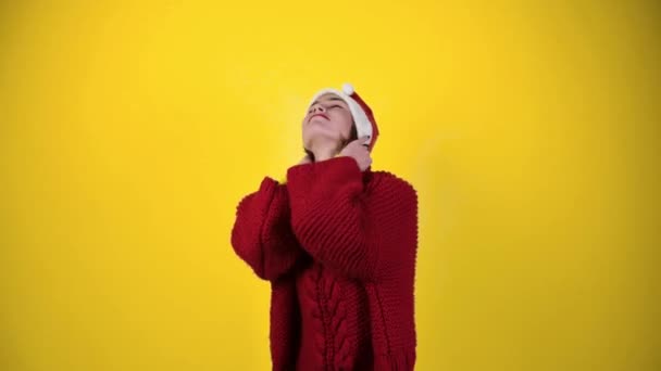 Junge positive Frau mit Weihnachtsmütze auf gelbem Hintergrund. Fröhliche junge Frau mit Weihnachtsmütze tanzt. Menschen und Winterurlaubskonzept - Filmmaterial, Video