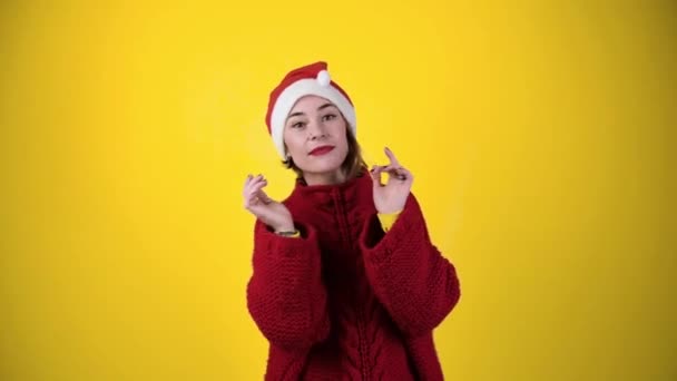 Fiatal pozitív nő karácsonyi Mikulás kalap elszigetelt sárga háttér. Boldog fiatal nő télapó kalapban táncol. Emberek és téli ünnepek koncepciója - Felvétel, videó