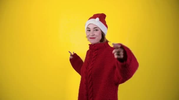 Młoda pozytywna kobieta w świątecznym kapeluszu odizolowana na żółtym tle. Szczęśliwa młoda kobieta w kapeluszu Mikołaja tańczy. Koncepcja ludzi i ferie zimowe - Materiał filmowy, wideo