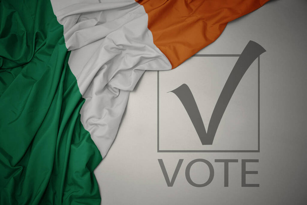махаючи барвистим національним прапором Ірландії на сірому фоні з текстовим голосуванням. концепція виборів. 3D ілюстрація
 - Фото, зображення