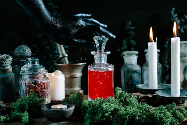 mão bruxa preta abrindo poção mágica, ervas ingredientes velas e equipamentos mágicos - Foto, Imagem