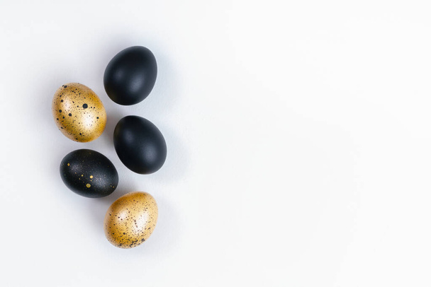 Eggs painted gold and black on white background. Minimal Easter concept. Golden luxury backdrop with copy space for text. - Фото, изображение