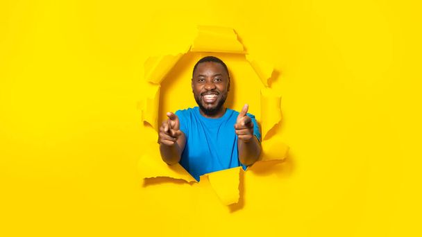 Ja mitä sinussa on. Onnellinen afrikkalainen mies osoittaa kameraa sormella ja hymyilee, murtautuu läpi keltaisessa paperissa olevasta reiästä, mies valitsee ja osoittaa: - Valokuva, kuva