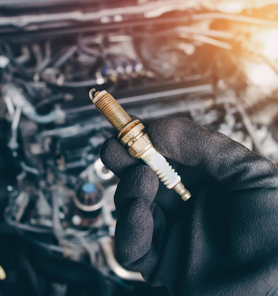 Automobile iridium spark plugs holds by auto mechanic hand with engine compartment blurred background and sunlight. - Photo, image