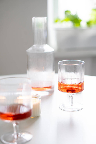 Rózsaszín bor trendi bordás borosüvegben és dekanter fehér asztalon, hétvégi házi borparti gyertyákkal közelkép - Fotó, kép