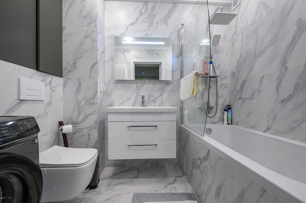 Moderno baño de mármol blanco interior con asiento de inodoro, lavadora y bañera - Foto, Imagen