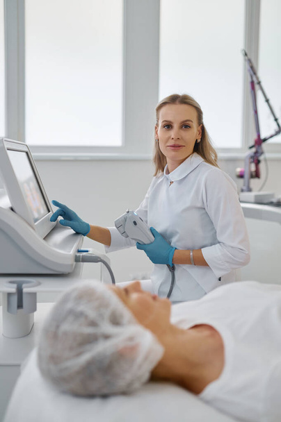 Retrato de cosmetóloga femenina trabajando con máquina láser en consultorio médico moderno. Concepto cosmetológico profesional - Foto, imagen