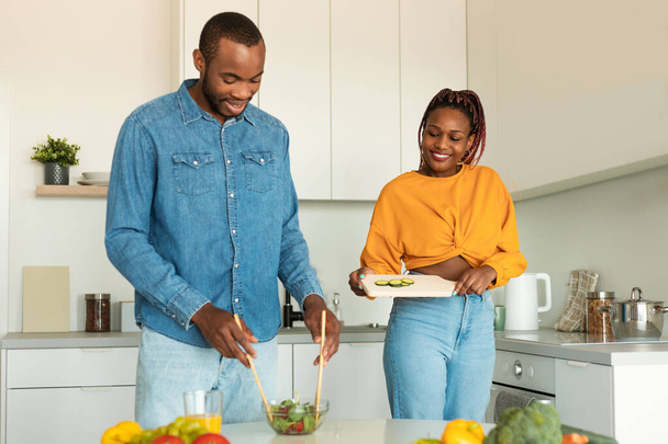 Afro-Amerikaans echtpaar koken samen in de moderne keuken, genieten van het bereiden van het diner, familie salade thuis. Voeding, koken, gezonde recepten - Foto, afbeelding