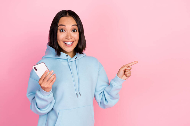 Photo of funny impressed girl dressed blue sweatshirt writing sms modern gadget pointing empty space isolated pink color background. - Foto, Bild