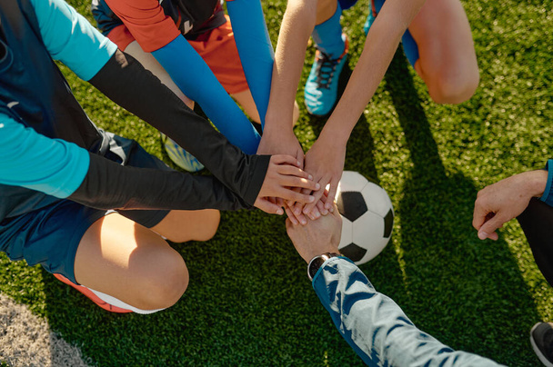 Football coach motivating junior football team before match stacking hands on ball together - Φωτογραφία, εικόνα
