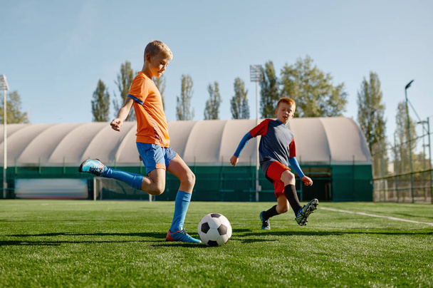 Πορτρέτο του σχολείου αγόρια προπόνηση ποδοσφαίρου στο γήπεδο ποδοσφαίρου. Δύο παιδιά επιτιθέμενος και αμυντικός τρέχει με μπάλα - Φωτογραφία, εικόνα