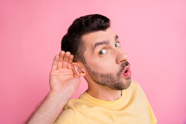 Portrait of curious astonished funny man stylish haircut yellow t-shirt arm on ear listen secret isolated on pink color background. - Photo, image