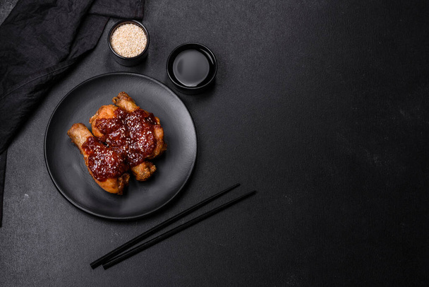 Tasty spicy chicken legs with teriyaki sauce and sesame seeds on a dark concrete background - Foto, Imagem