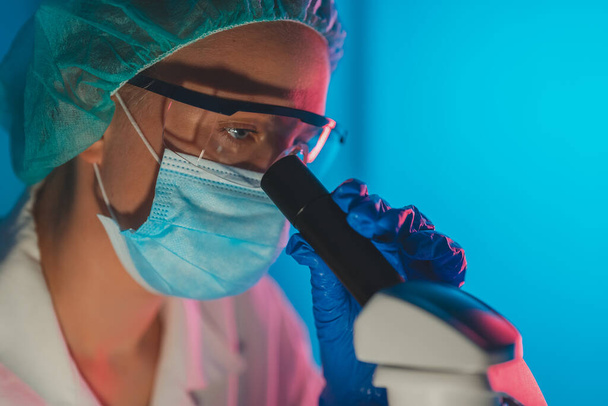 Wetenschapper in medisch masker werkt met microscoop in het lab. - Foto, afbeelding