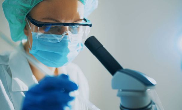 Επιστήμονας στην ιατρική μάσκα που εργάζεται με μικροσκόπιο στο εργαστήριο. - Φωτογραφία, εικόνα