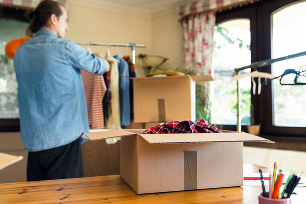 Box with pre owned clothes for resale or donation, unfocused man on background preparing the clothes. - 写真・画像
