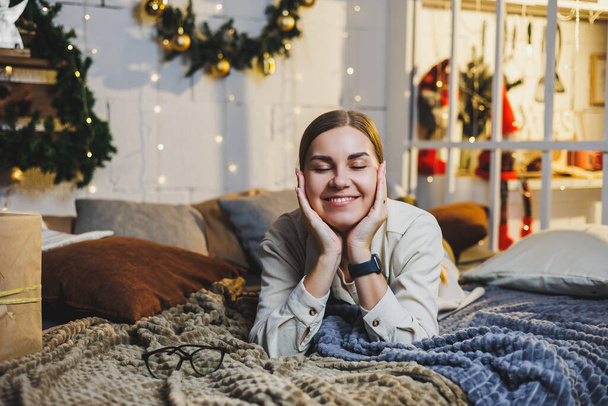 Portrait d'une femme souriante heureuse sur fond de décorations du Nouvel An. La femme est heureuse avec les vacances de Noël. Ambiance du Nouvel An à la maison - Photo, image