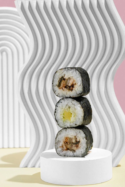Ασιατική κουλτούρα, γιαπωνέζικο χοσομάκι (σούσι, ρολά) με χέλι σε ροζ και κίτρινο φόντο. Ανατολική μαγειρική, ανατολική μαγειρική. Νόστιμα ορεκτικά στο πιάτο - Φωτογραφία, εικόνα