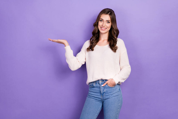 Фото молодой деловой леди носить белый свитер хороший джинсы джинсы держать ладонь демонстрации дешевый продукт цены изолированы на фиолетовом фоне цвета. - Фото, изображение