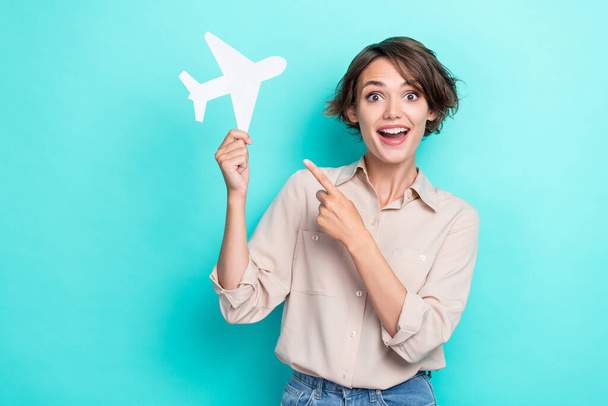 Photo of young charming positive businesswoman excited finger pointing white paper airplane positive mood flight travel isolated on cyan color background. - Foto, immagini