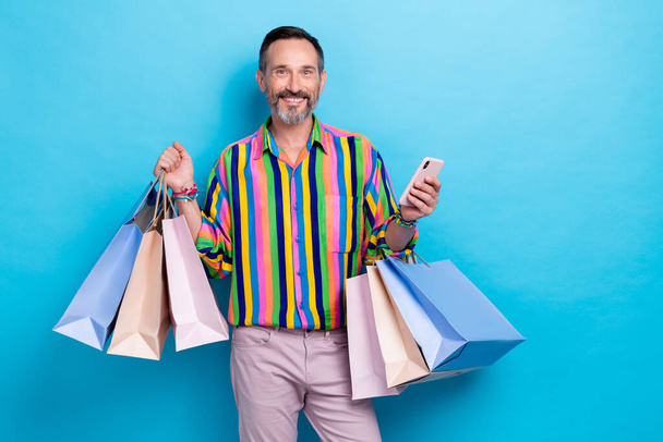 Photo of attractive man wear bright trendy outfit hold device choose vintge stylish clothes online isolated on blue color background. - 写真・画像
