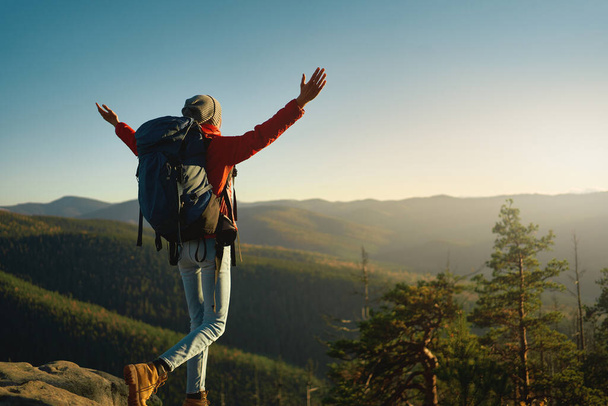 Woman hiker wih big backpack enjoying view of mountain summit with raising her arms up into the sky - Foto, Imagem