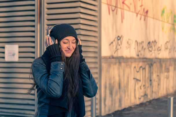 Beautiful young woman listening to music in the city streets - 写真・画像
