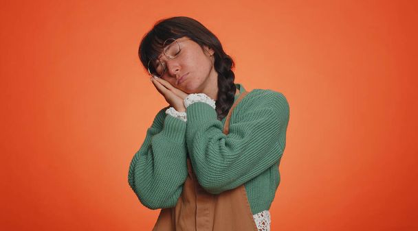 Tired lovely millennial woman in green sweater yawning sleepy inattentive feeling somnolent lazy bored gaping suffering from lack of sleep. Young nerd one girl isolated on orange studio background - Photo, Image