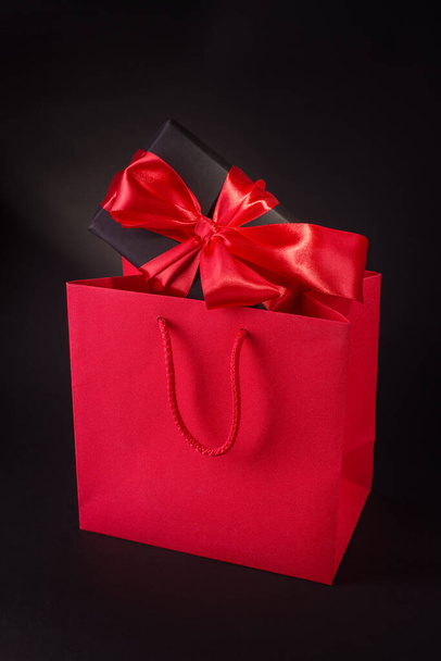 Hyvää ystävänpäivää tai Black Friday Shopping Concept Black Gift Box ja Red Satin Bow Against Black Background. Promo banneri kopioi tilaa. - Valokuva, kuva