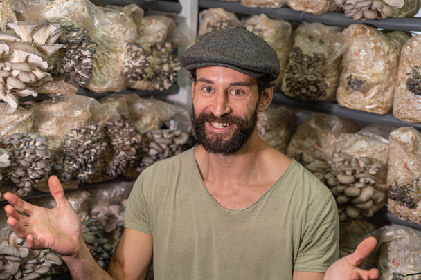 Portret podekscytowanego właściciela hodowli grzybów ostrygowych. młody człowiek uśmiechnięty do kamery na tle bloków rodukcyjnych grzybów ostryg - Zdjęcie, obraz