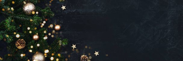 Banner with Christmas tree branches, golden baubles and pine cones on black background with Christmas bokeh lights. New Year concept. Top view, copy space. - Photo, Image