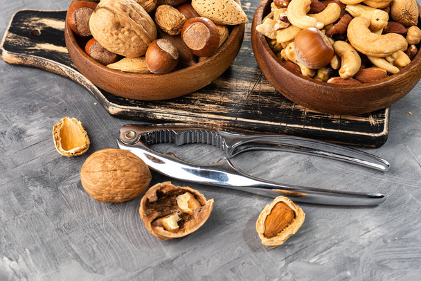 Various nuts in a wooden bowl on gray table and a nut cracker.  Close-up of a walnut. Space for text. - Фото, зображення
