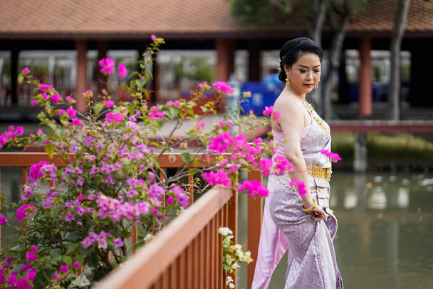 A woman in a traditional Thai costumes is standing on the wooden bridge while being taken a portrait photo shooting. - Photo, image