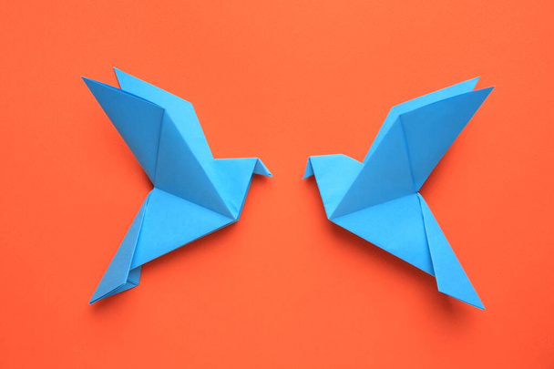 Beautiful light blue origami birds on orange background, flat lay - Фото, изображение