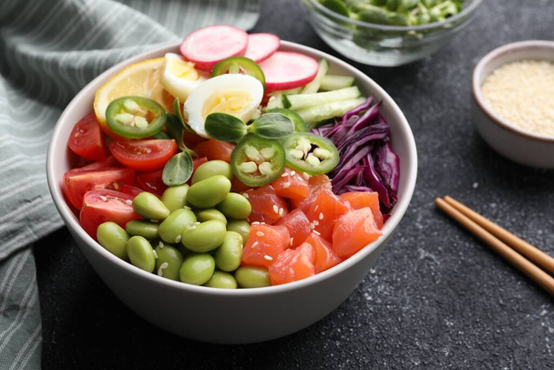 Poke bowl with salmon, edamame beans and vegetables on black table - 写真・画像