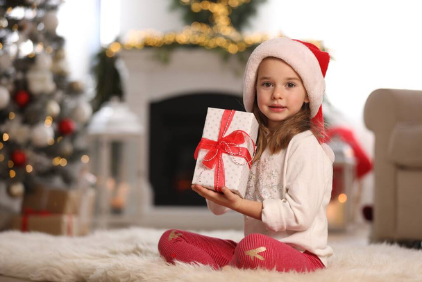 Cute little girl holding gift box in room decorated for Christmas - Photo, image