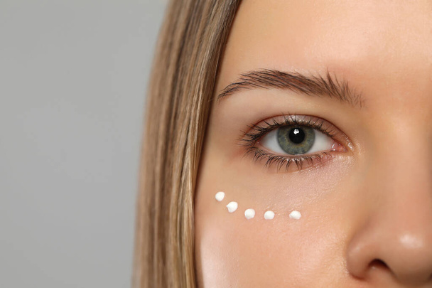 Young woman with cream around eye on light grey background, closeup. Space for text - Photo, image