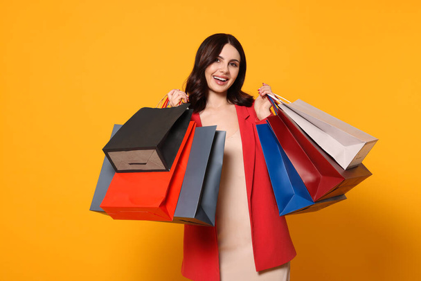 Beautiful young woman with paper shopping bags on yellow background - Foto, imagen