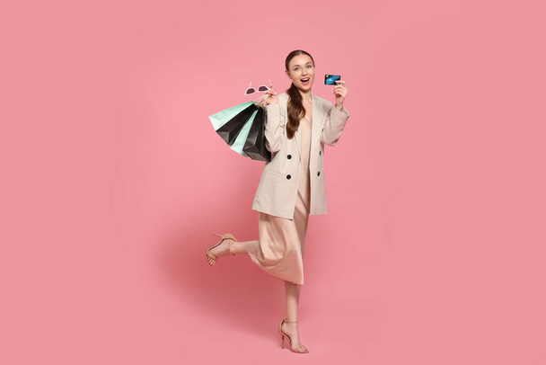 Stylish young woman with shopping bags and credit card on pink background - Foto, immagini