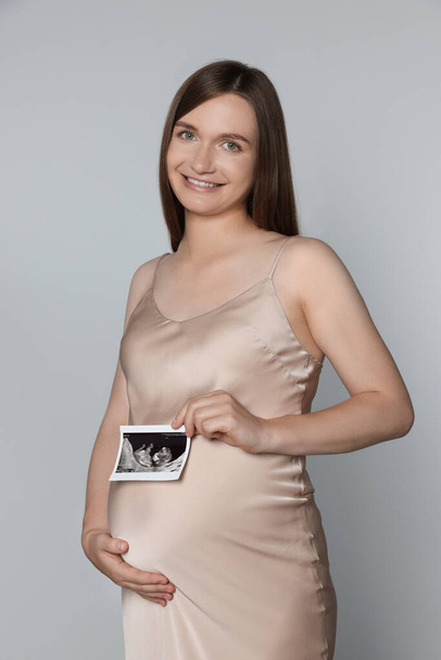 Pregnant woman with ultrasound picture of baby on light grey background - Photo, Image