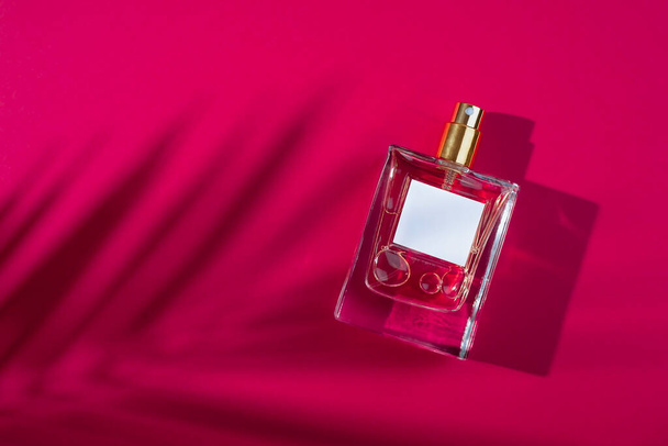 Transparent bottle of perfume with label on a red background. Fragrance presentation with daylight. Trending concept in natural materials palm leaves shadow. Womens and mens essence. - Valokuva, kuva