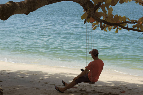 Υπέρυθρη εικόνα ενός άγνωστου άνδρα που κάθεται μόνος του στον πάγκο με το σχοινί να αιωρείται κάτω από το δέντρο - Φωτογραφία, εικόνα
