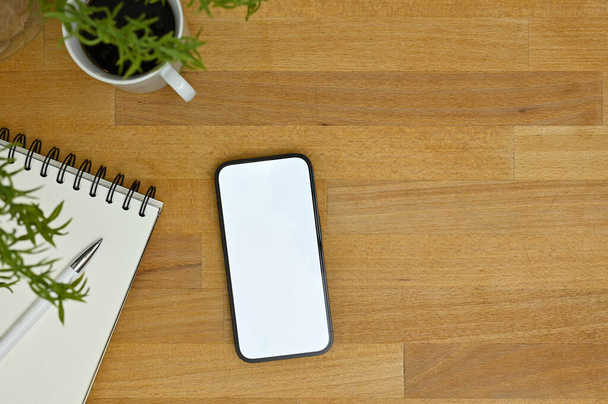 Widok z góry, Smartfon biały ekran makieta z spiralnym notatnikiem i filiżanka kawy na drewnianym blat. - Zdjęcie, obraz