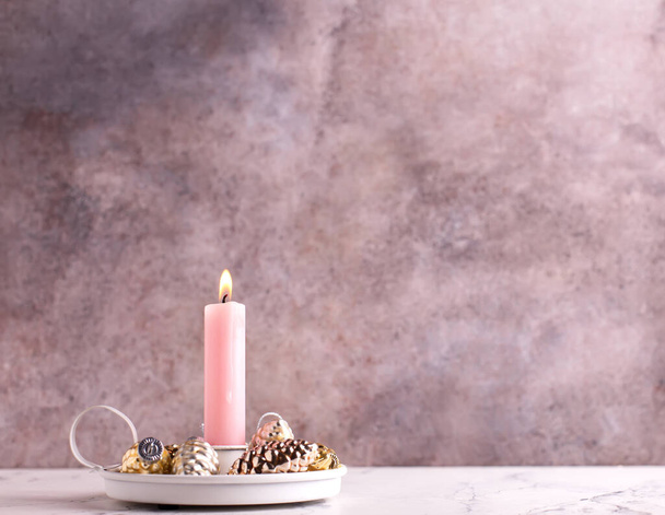 Pink burning candle and golden  and golden and silver decorative cones against pink textured wall. Selective focus is on candle. Place for text. Pink Christmas postcard. - Fotoğraf, Görsel