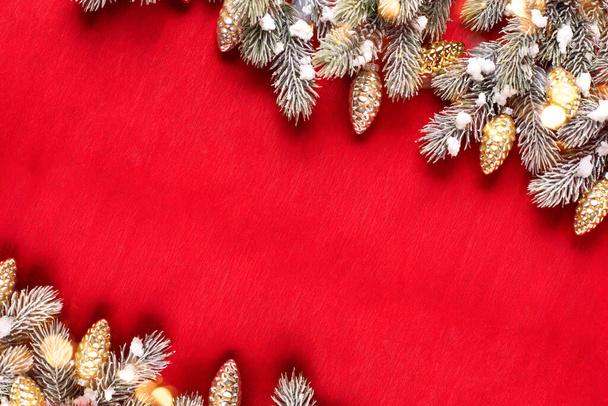Frame van takken van dennenboom en decoratieve gouden kegels op rood papier textuur achtergrond. Bovenaanzicht. Kerstmis, New Tear vakantie concept. Plaats voor tekst - Foto, afbeelding